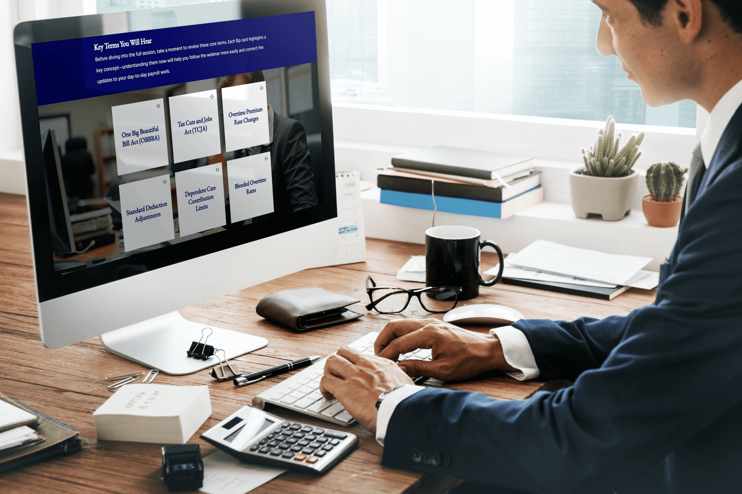 A person in business attire works at a desktop computer displaying a training module titled “Key Terms You Will Hear.” The screen shows a grid of interactive cards with payroll and tax-related terms such as One Big Beautiful Bill Act (OBBBA), Tax Cuts and Jobs Act (TCJA), Overtime Premium Rate Changes, Standard Deduction Adjustments, Dependent Care Contribution Limits, and Blended Overtime Rates. The desk has office supplies, books, a calculator, a wallet, glasses, and a coffee mug, with potted plants.