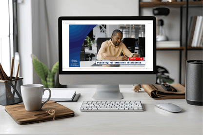 A computer screen displays a man writing, titled “Planning for Effective Instruction.” The desk holds coffee, notebooks, and a plant, evoking a calm, productive workspace.