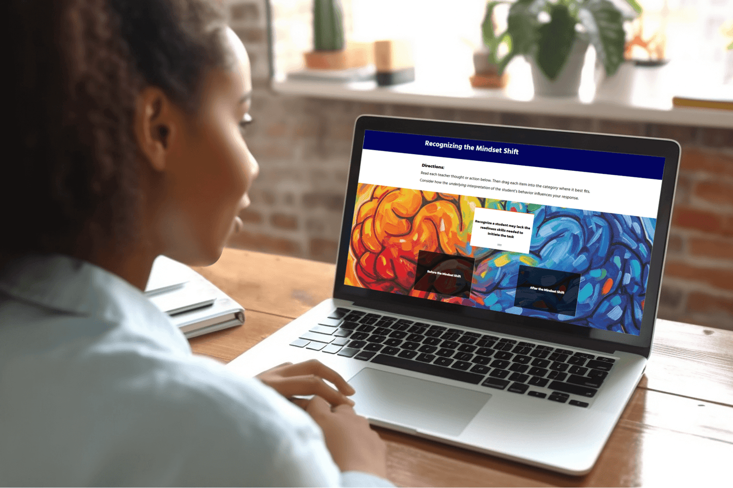 A woman sits at a wooden desk using a laptop. The screen displays colorful abstract art and text about "Recognizing the Mindset Shift," and an interactive activity of dragging the activity to the correct Mindset Shift. 