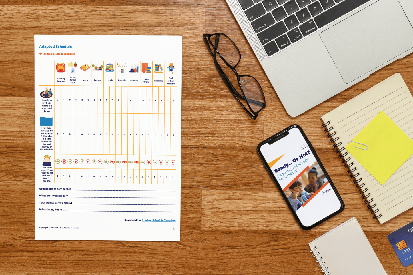 Workspace with a wooden desk featuring a printed Adapted Schedule, glasses, a laptop, notebook, and smartphone displaying "Ready Or Not?" presentation.
