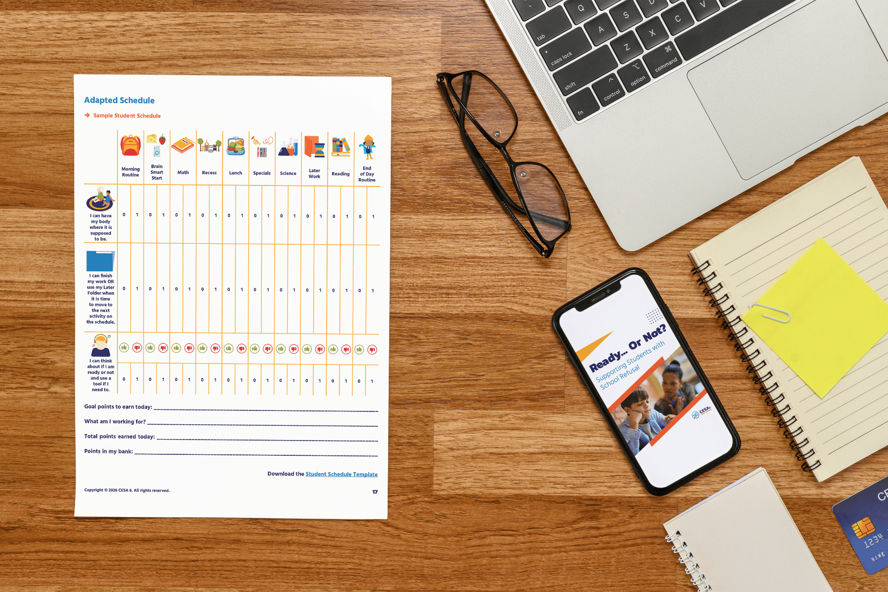 Workspace with a wooden desk featuring a printed Adapted Schedule, glasses, a laptop, notebook, and smartphone displaying "Ready Or Not?" presentation.