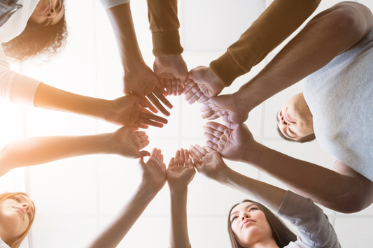 A diverse group of people standing in a circle, reaching their hands toward the center and joining them together, symbolizing teamwork and unity. 