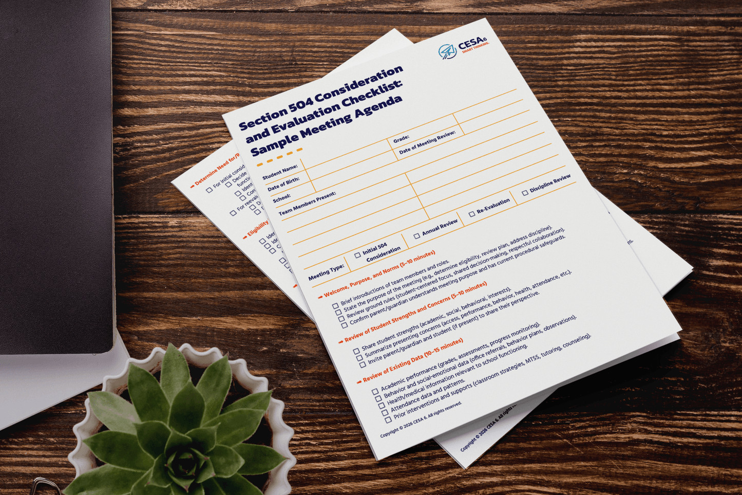 Two printed documents titled "Section 504 Consideration and Evaluation Checklist" lie on a wooden table. A succulent and a closed laptop are nearby, creating an organized and professional atmosphere.