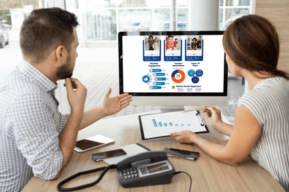 A man and woman discuss data displayed on a desktop screen showing graphs and charts. The setting is an office with a focused, collaborative atmosphere.