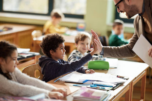 The image features a classroom scene where a teacher and a student are exchanging a high-five, indicating a positive and encouraging interaction.