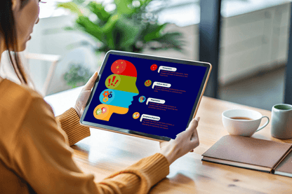 A woman views a tablet displaying a colorful infographic of a human head silhouette with icons and text bubbles, in a bright, modern setting with a coffee cup nearby.