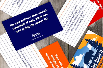 A collection of colorful motivational cards scattered on a wood surface. The central card reads, "Do you believe this about yourself? If not, what are you going to do about it?" in bold white text on a dark blue background. Other cards feature handwritten and printed inspirational messages in varied colors, set against a mix of lined, orange, and scenic backgrounds. The overall tone is encouraging and reflective.