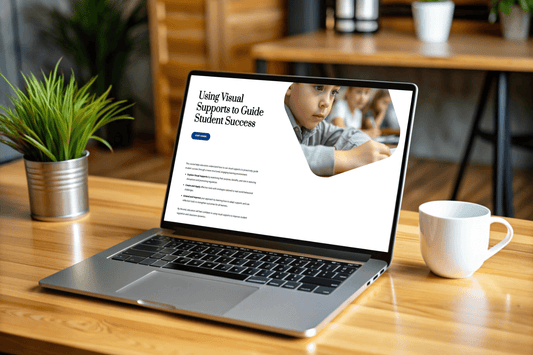 A laptop on a wooden desk displays a website titled "Using Visual Supports to Guide Student Success" with a young child in focus. The setting is calm and cozy, with a plant and coffee cup nearby.