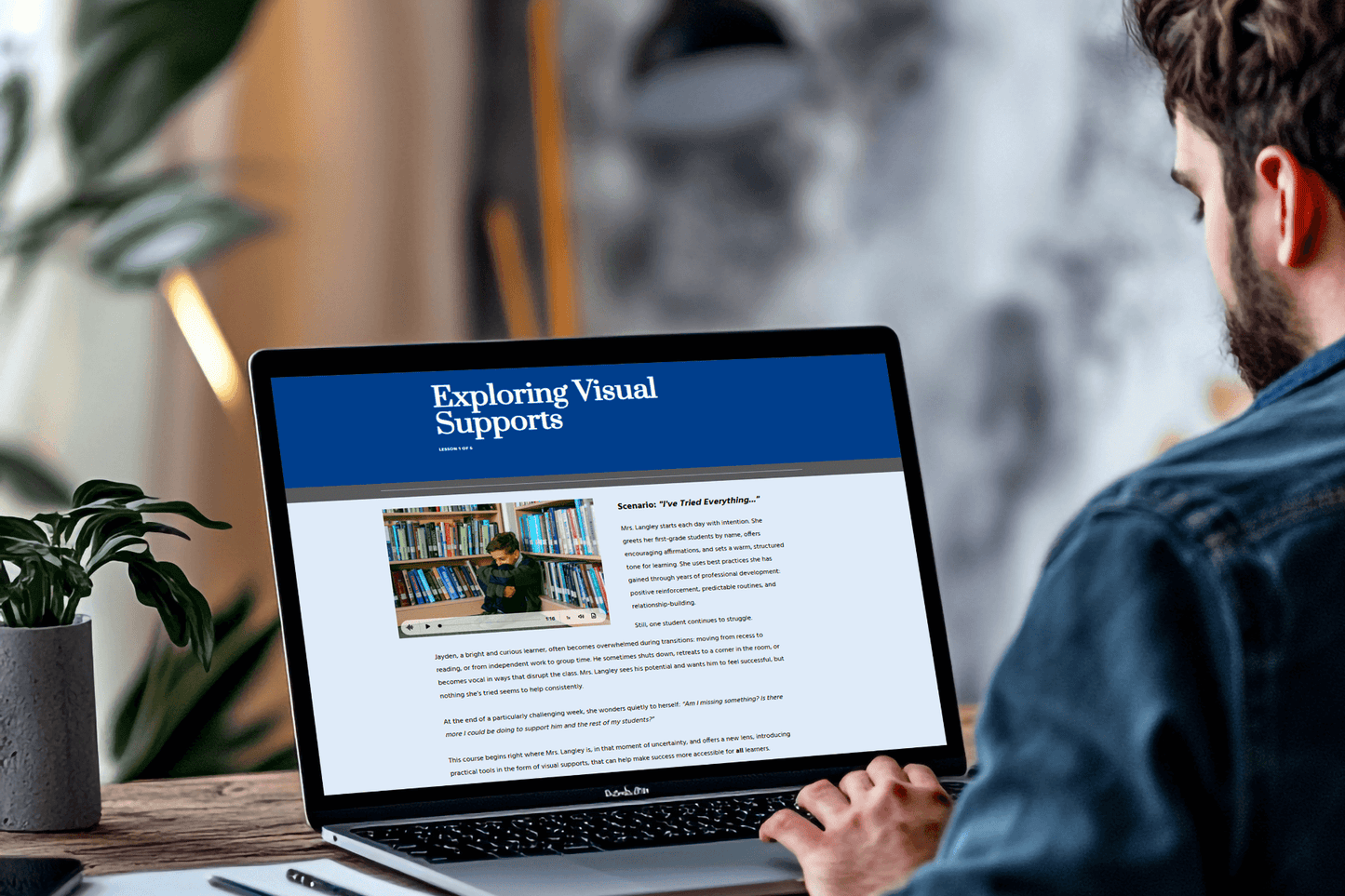 A person is using a laptop displaying a webpage titled "Exploring Visual Supports." The screen shows text and an image with audio of the scenario of a student by bookshelves. 