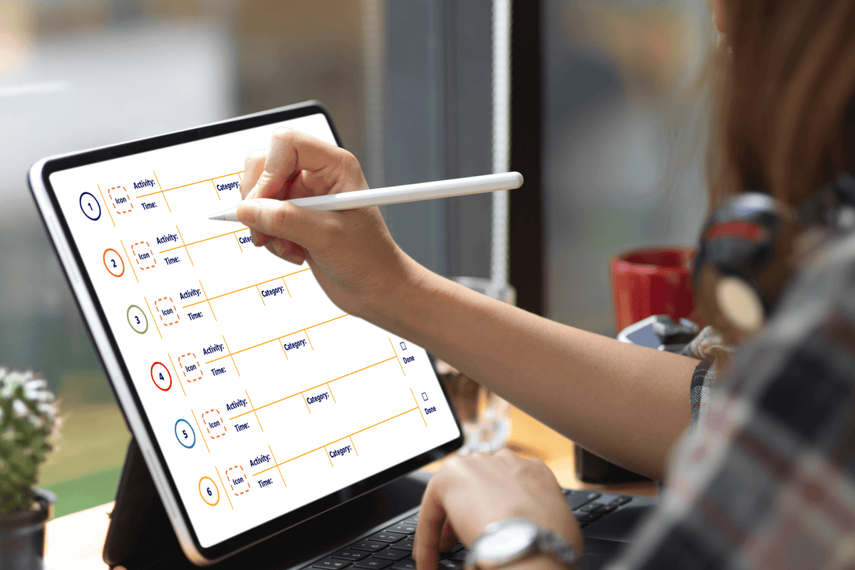 A person uses a stylus to update a color-coded schedule on a tablet at a desk, with a window and coffee mug nearby; the mood is calm and focused.