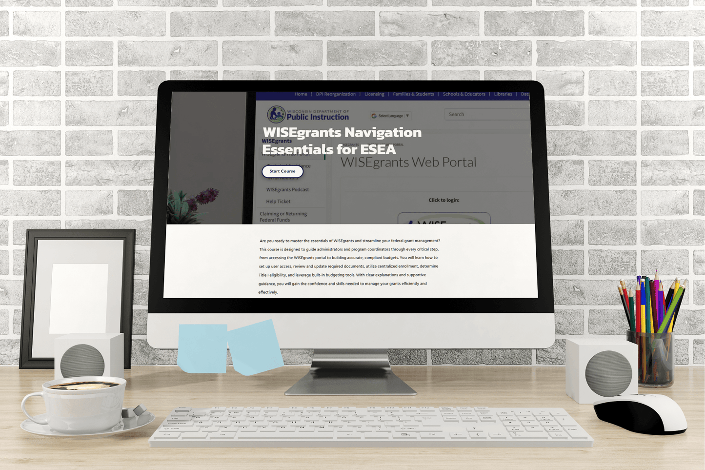 A desktop computer on a wooden desk displays a webpage titled "WISEgrants Navigation Essentials for ESEA." The scene includes speakers, a framed photo, pencils, a cup of coffee, and sticky notes, with a brick wall in the background, creating a productive and organized workspace atmosphere.