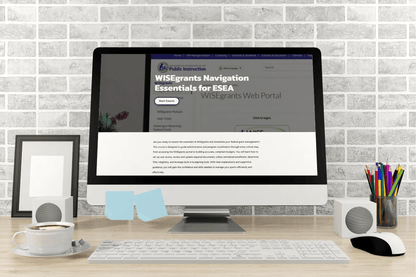 A desktop computer on a wooden desk displays a webpage titled "WISEgrants Navigation Essentials for ESEA." The scene includes speakers, a framed photo, pencils, a cup of coffee, and sticky notes, with a brick wall in the background, creating a productive and organized workspace atmosphere.