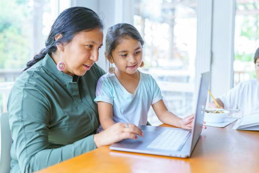 The image shows a mother and daughter using a laptop together, focused on the screen in a cozy indoor setting.