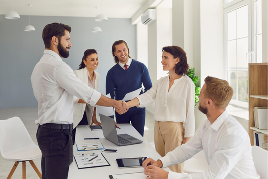 Professional business meeting in a well-lit, accessible office space, featuring diverse colleagues engaging in a handshake and discussion. The environment promotes collaboration, inclusivity, and clear communication.